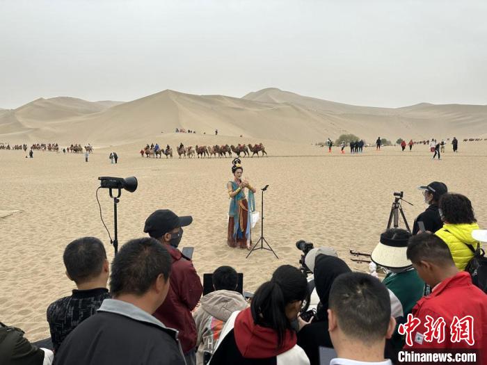 圖為2023年4月底，敦煌大漠“逐舞者”奧楠在鳴沙山月牙泉景區(qū)視頻直播，吸引游人圍觀?！●T志軍 攝